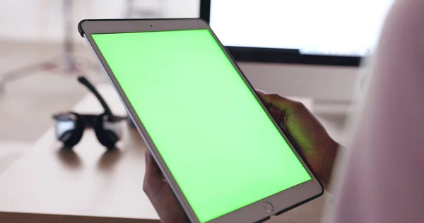 Close up of an African American persons hands holding a tablet with a plain green screen with a blurred background of headphones. Technician working out how to fix broken device. IT problem solving.