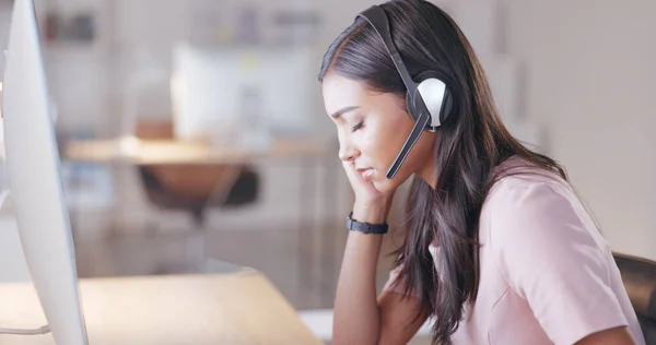 Young call center agent suffering from a headache or migraine while working in customer service. Support employee feeling tired, overworked and sick while wearing a headset at her desk in the office.