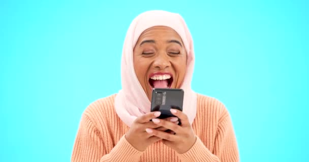 青の背景のモックアップに隔離されたスタジオでの顔 イスラム教徒の女性 受賞者とお祝い 宝くじ 賞品または競争に勝つための携帯電話を持つ成功 肖像画または興奮したイスラム教徒 — ストック動画