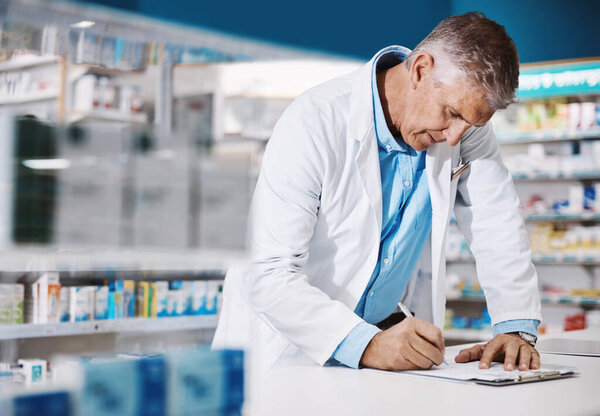 Checking a big prescription. a male pharmacist writing on a clipboard in a drugstore
