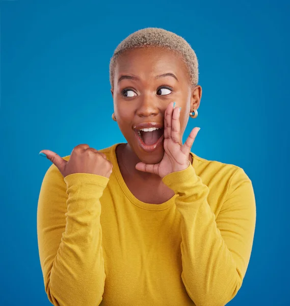 Black woman, gossip and secret in studio with hand on face for sale announcement. African female model on a blue background to whisper message, news information or wow rumor pointing at mockup deal.