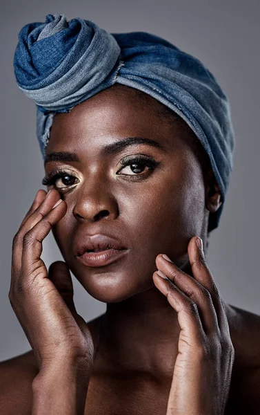 Glowing skin is a result of proper skincare. a beautiful young woman wearing a denim head wrap while posing against a grey background