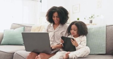 Laptop, tablet ve çocuklu anne uzaktan çalışma, kazanç ve oturma odasında kaliteli zaman geçirmek için birlikte kanepede oturuyorlar. İnternet, teknoloji ve kız kanepede öğrenilecek, gülümsenecek ve evden çalışacak.