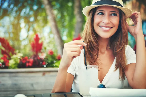 これはこれまでで最高の飲み物です 帽子をかぶって外のレストランに座って冷たい飲み物を楽しんでいる陽気な若い女性 — ストック写真