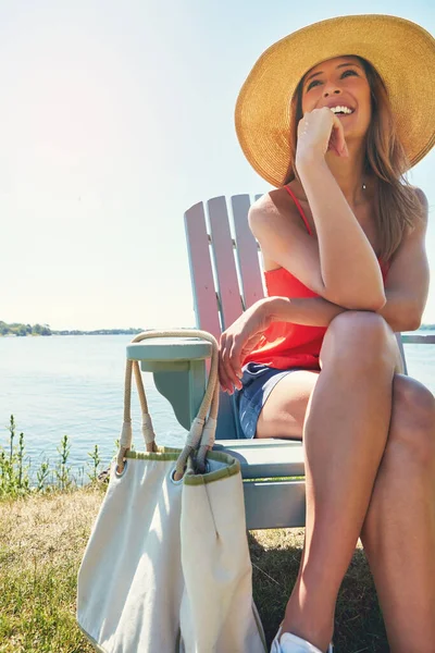 太陽を受け入れる 太陽の下で外の湖の隣の椅子に腰掛けながら帽子を被った明るい若い女性が — ストック写真