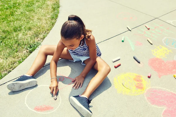 画她的杰作到处都是 一个可爱的小女孩在外面的人行道上用粉笔画画 — 图库照片