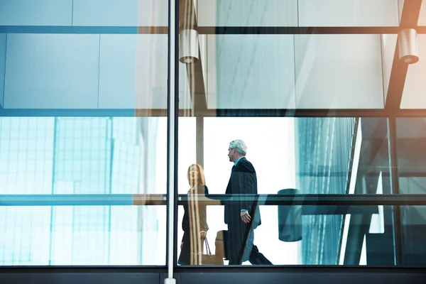 stock image They follow the path to success. a businessman and businesswoman walking and talking in a modern glass office