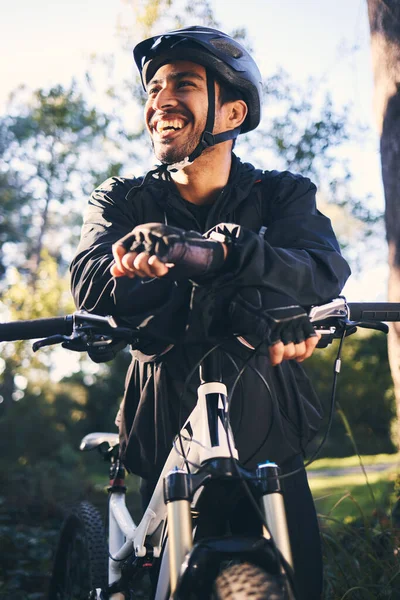 Forest, fitness and smile, cyclist on bicycle in nature with helmet, exercise adventure trail and healthy mindset. Cycling, relax and man with mountain bike in trees for workout, motivation or energy.
