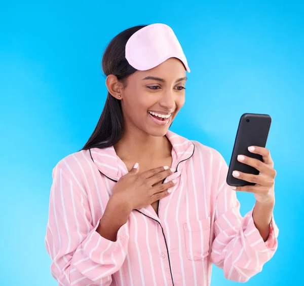 Wow, phone and pajamas with a woman on a blue background in studio browsing social media in the morning. Mobile, contact and gossip with an attractive young female reading good news while texting.