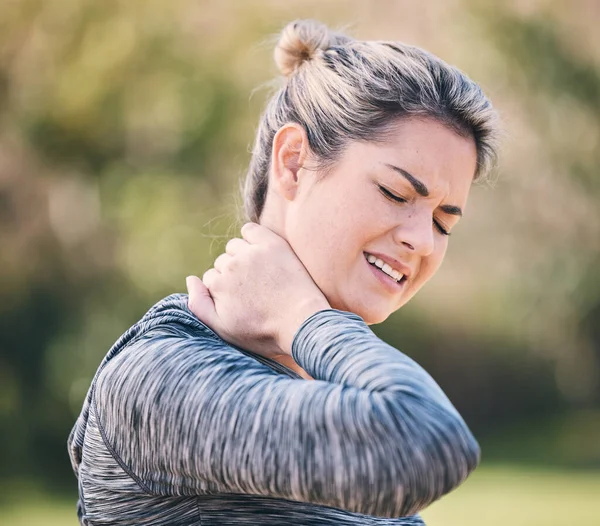 Fitness, injury and woman with neck pain in a park during running routine on blurred background. Spine, problem and girl suffering from injured muscle, arthritis or shoulder strain after workout run.
