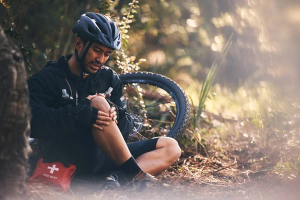 Man, cycling and outdoor with leg or knee injury in nature for sports, exercise or training on mountain bike. Athlete person with bicycle and first aid for fitness workout accident or fall in forest.
