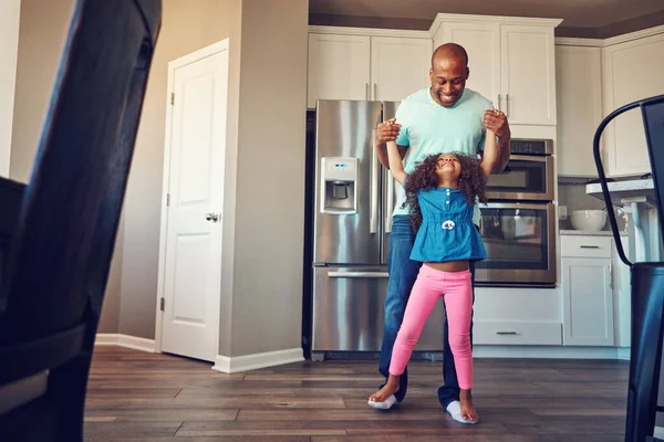 Taking strides together. a happy little girl balancing on her fathers feet while they walk around in the kitchen together