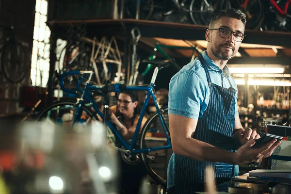 To make profit youve got to plan for it. a mature man using a calculator in a bicycle repair shop with his coworker in the background