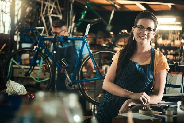 Lets restore your bike to its former glory. Portrait of a young woman working in a bicycle repair shop with her coworker in the background