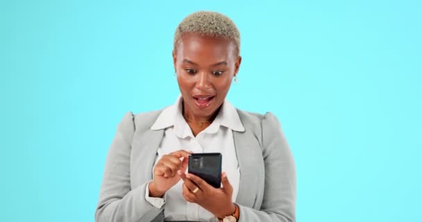 ソーシャルメディア インターネット モバイルアプリのための電話で青の背景に驚き すごいと黒の女性 コミュニケーション チャットのためのスマートフォン上の勝者と女の子 スタジオでの勝利とオンラインボーナス — ストック動画