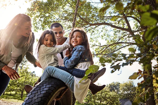 家族の思い出を作る 幸せな母親と父親が娘たちをタイヤスイングに押し込み — ストック写真