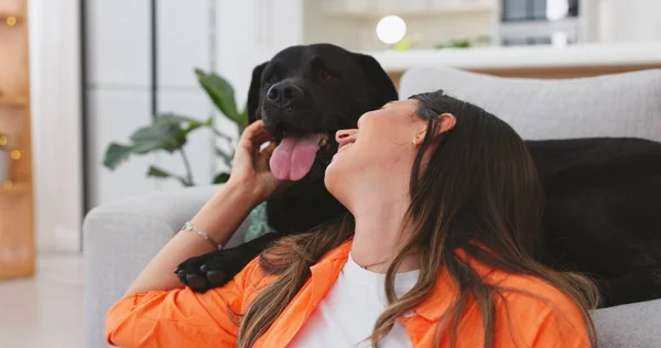 Happy woman relax with her dog at home for mental health, wellness or emotional support, love and care. Young person sitting on living room floor and pet, animal or Labrador retriever kiss and stroke.