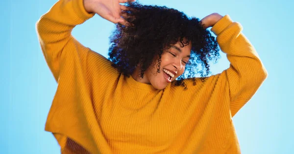 Happy black woman, dance and beauty in studio by blue background for fashion, smile or wellness. Young gen z student, dancing and freedom with yellow clothes, curly hair afro and fitness by backdrop.