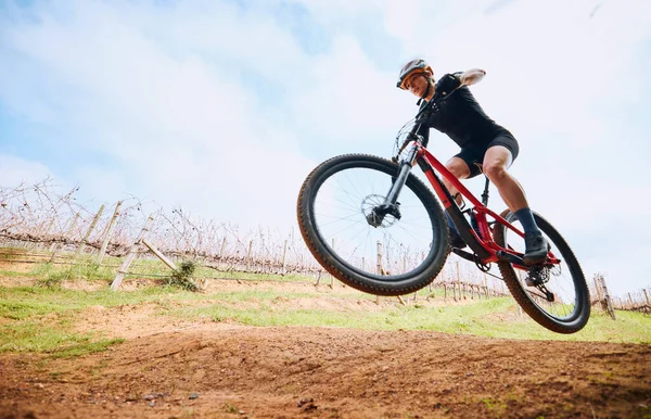 Bicycle jump, countryside and woman on a bike with speed for sports on a dirt road. Fitness, exercise and fast athlete doing sport training in nature on a park trail for cardio and cycling workout.