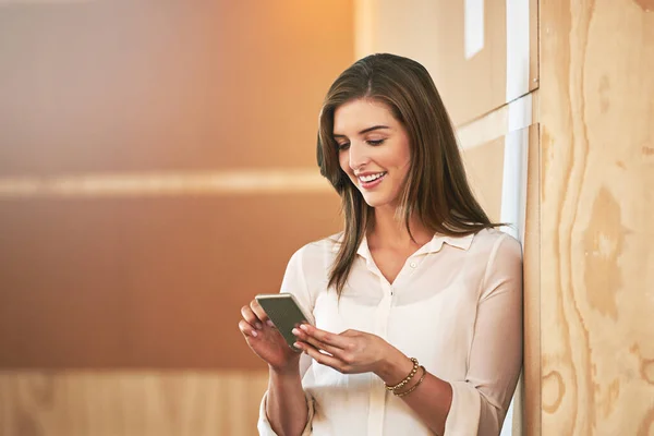 stock image Taking a time out from her work. a smiling young woman using her cellphone while standing in an office