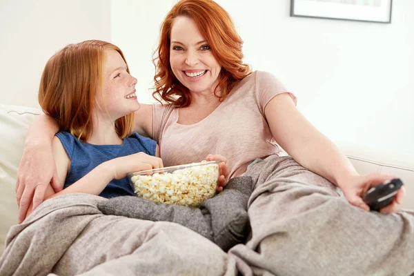 She picked tonights movie. a mature woman and her young daughter watching a movie and eating popcorn on the sofa