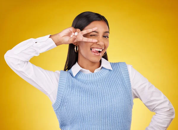 Peace sign, hands and portrait of Indian woman wink in studio for happiness, confident and fashion. Emoji mockup, yellow background and girl with hand gesture for joy, positive mindset and happy.