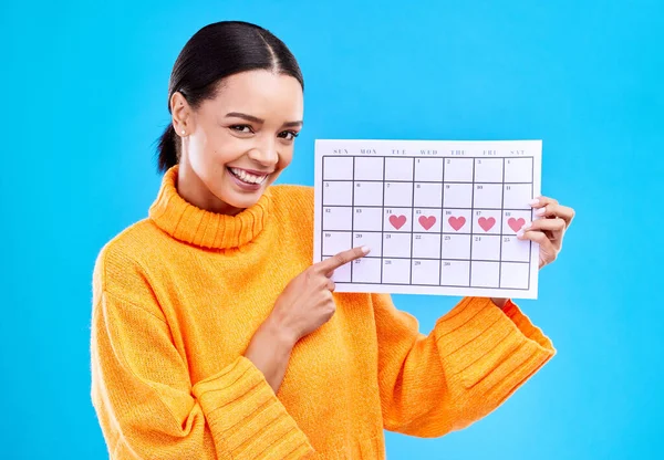 Health, portrait and female with a calendar in a studio to track her menstrual or ovulation cycle. Happy, smile and face of a woman model pointing to a paper period chart isolated by blue background