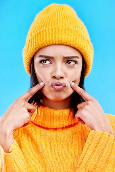 Quirky, goofy and young female in a studio with a comic, funny and crazy face expression. Gen z, silly and beautiful woman model from Puerto Rico touching her cheeks isolated by a blue background