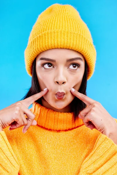 Goofy woman in winter fashion with comic expression, beanie and fun isolated on blue background. Style, happiness and silly gen z girl in studio with funny face and warm clothing for cold weather