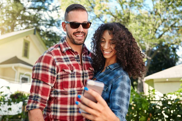 stock image Thats a really nice one of us. a young couple standing outside looking at something on a cellphone