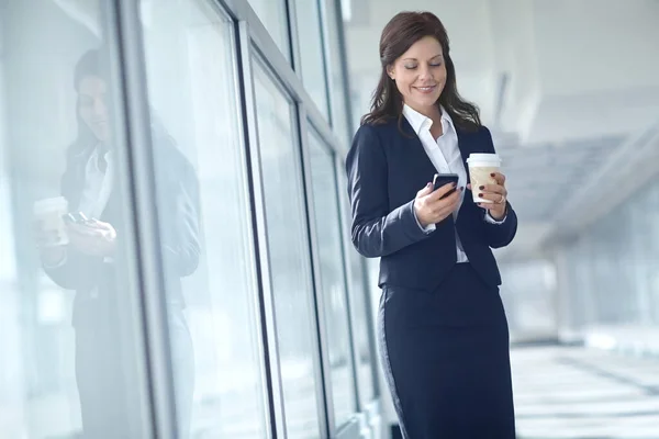 1人の実業家か弁護士はオフィスでコーヒーの持ち帰り再利用可能なコップを持っている間彼女の携帯電話でテキストを送る 休憩中にインターネットを閲覧する企業の笑顔 — ストック写真