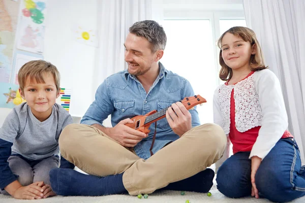 stock image Dad always makes time to play. a happy father playing the guitar for his son and daughter at home