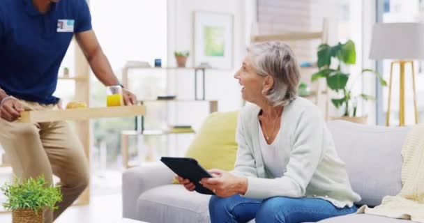 辅助生活和退休与一个老年妇女在沙发上的客厅里的家 食物和一名黑人护士在护理机构为一位老年病人提供膳食 — 图库视频影像