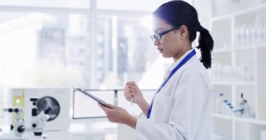 Serious female scientist working and writing patient information in a lab. Laboratory worker looking at and analyzing health data for a science journal. Medical professional doing a clinical trial.