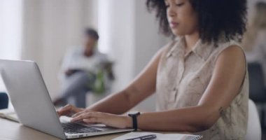 Young business woman typing on a laptop while sitting at a desk in her office. Creative professional with an afro typing an email and smiling at her job. Confident woman focused on sending an email.