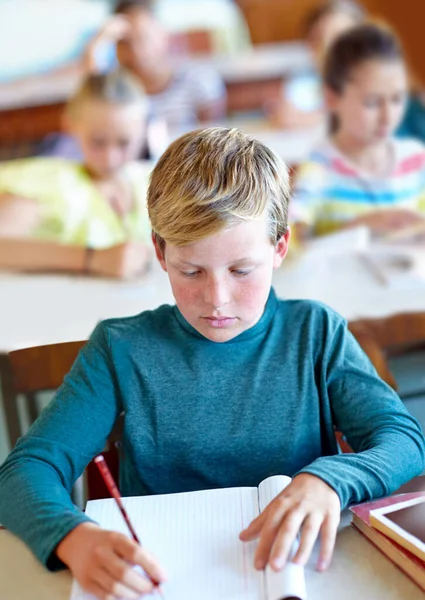 他是个勤奋的学生 一个在课堂上在笔记本上写字的小男孩 — 图库照片