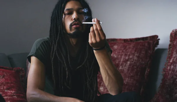 stock image Under the influence. a young man smoking a marijuana joint at home