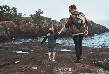 Eve kadar tüm yolu atlamak. Neşeli bir baba ve oğulun gün boyunca okyanusun yanında yürürken el ele tutuşmalarının dikiz görüntüsü.