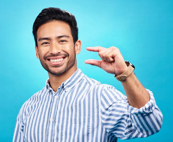 Small, hand and gesture of a man portrait with a smile in studio showing a tiny measurement. Isolated, blue background and Asian model with happiness, positive opinion and hands show of pinch size.