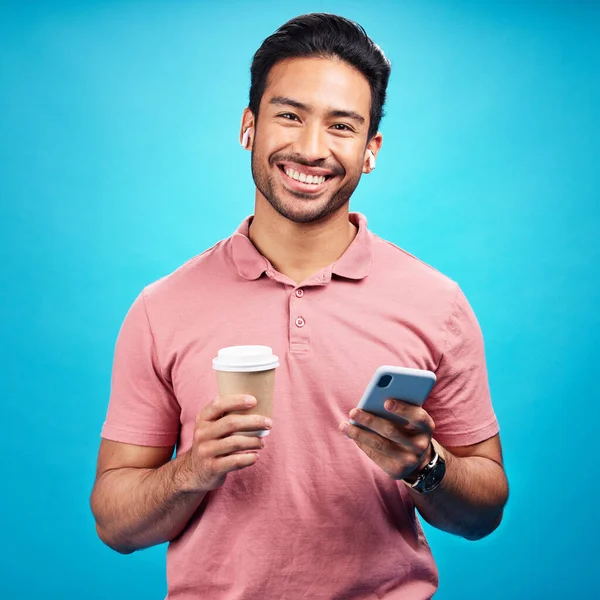 スタジオで電話を持つ男のイヤフォン コーヒー 肖像画は 青い背景に隔離されています アジア人のお茶 携帯電話と幸福飲料 カフェインとソーシャルメディア 音楽やラジオ用の携帯電話 — ストック写真