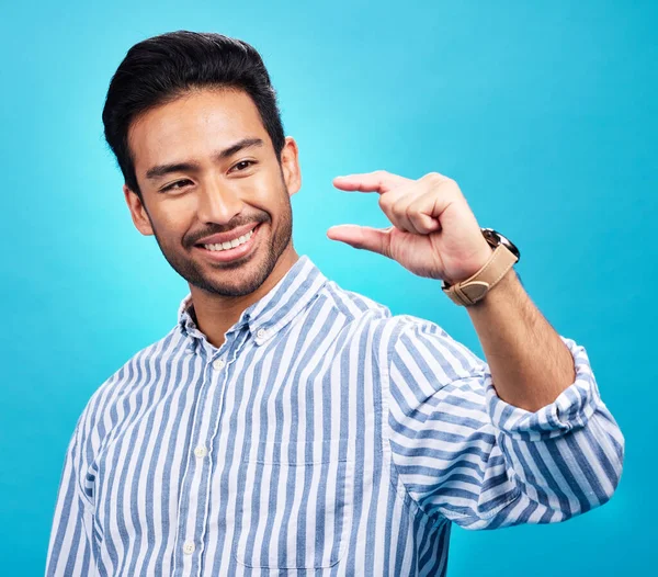 Small, hand and gesture of a man with a smile in studio showing a tiny measurement. Isolated, blue background and male model show happiness and positive opinion with hands from small size sign.