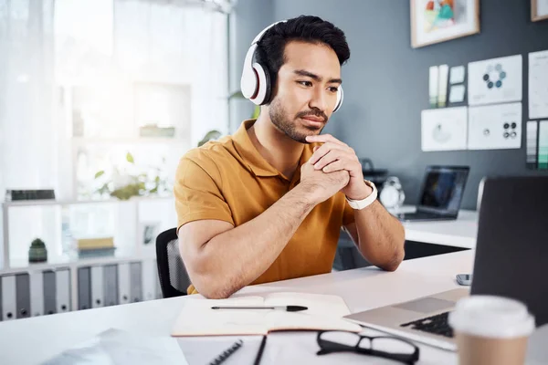 Thinking, laptop and headphones on business man listening to music, audio or webinar. Asian male entrepreneur with technology for planning strategy, idea or reading email or communication on internet.
