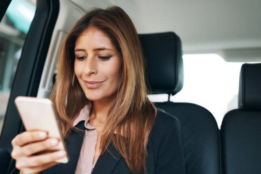 Gelişmelerden haberdar olmak. Olgun bir iş kadını bir arabanın arka koltuğunda cep telefonu kullanıyor.