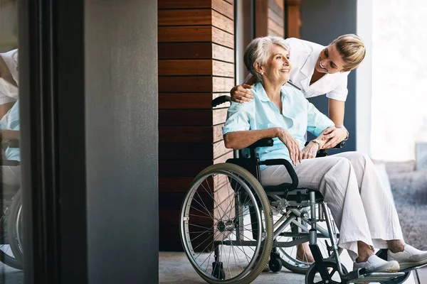 You can tell she cares deeply about her patients. a nurse caring for a senior patient in a wheelchair outside a retirement home