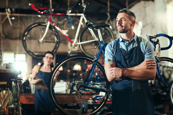 自行车是他的生意 在自行车修理店工作的一个成熟的男人 背后有他的同事 — 图库照片