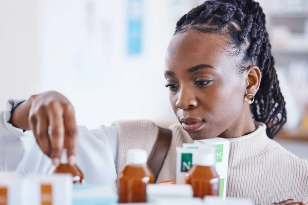 Serious black woman, patient and medication on shelf for cure, illness or pain relief at pharmacy. African American female reading or looking at pharmaceutical products, medicine or drugs at clinic.