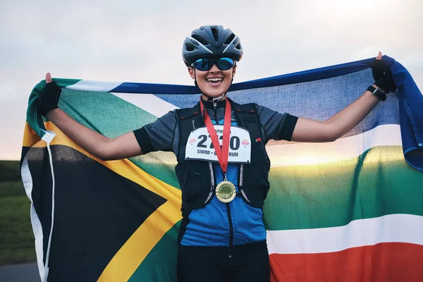 Winner sports, happy woman from South Africa with flag and gold medal winning, outdoor cycling race or triathlon. Happiness, win and cyclist with smile, fitness and world record with national pride