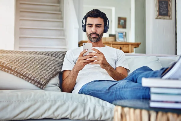这就是他休假的方式 用电话和耳机在沙发上休息的男人 — 图库照片