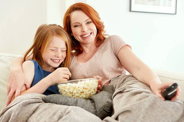 stock image We love all the same movies. a mature woman and her young daughter watching a movie and eating popcorn on the sofa