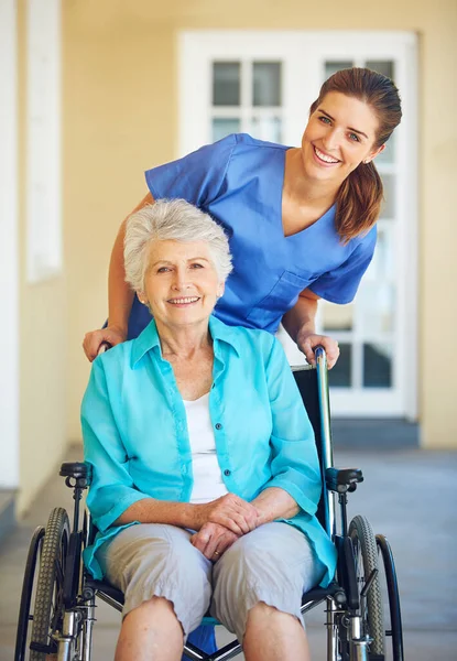 我的医生有一颗金子般的心 一位医生把她的老年病人推上轮椅 — 图库照片